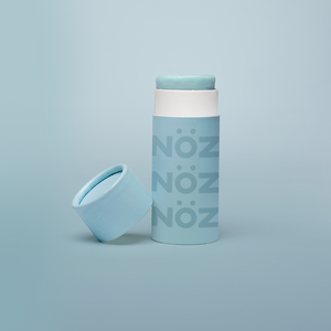 Blue Nöz sunscreen stick with cap off, tilted against base of stick. All against a pale blue gradient background. 