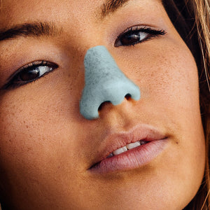 Young woman with chiseled cheekbones, dark hair & eyes, and olive skin wearing the blue Nöz sunscreen stick. 