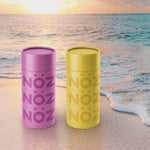 Load image into Gallery viewer, Purple and yellow Nöz sunscreen sticks against an ocean and sand background at sunset. 
